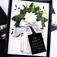 a vase with flowers in it and a card attached to the frame next to it