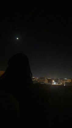 a person standing in the dark with their back turned to the camera, looking out over a city at night