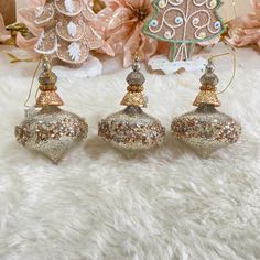 three christmas ornaments sitting on top of a white fur covered floor next to pink flowers