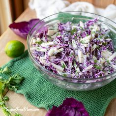 a glass bowl filled with coleslaw on top of a green cloth next to a lime