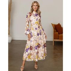 a woman in a floral print dress standing next to a white wall and brown chair