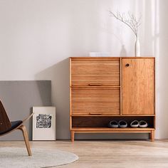 a wooden cabinet sitting next to a chair in a living room with white walls and wood flooring