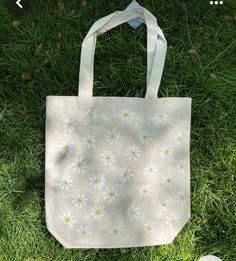 a white bag with yellow and white flowers on it sitting in the grass next to a pair of scissors