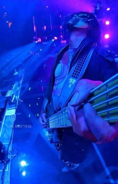 a man playing an electric guitar in front of purple and blue lights at a concert