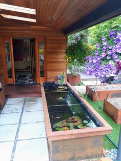 a fish pond in the middle of a patio with purple flowers on the other side