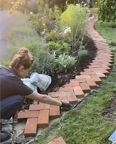 a woman laying bricks on the ground in front of some plants and flowers near a brick path