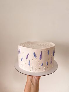 a hand holding a white cake with blue flowers on it and the frosting has purple sprinkles