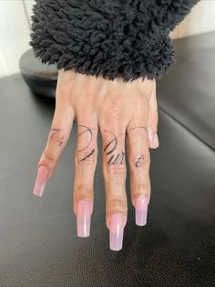 a woman's hand with pink nails and tattoos on her left thumb, next to a black table