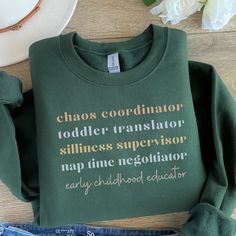 a green sweatshirt that says chaos coordinater toddler transslatoor stillness supervisor nap time necotator easy childhood education