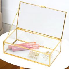 a pink lipstick sitting inside of a glass box on top of a table next to a pair of earrings