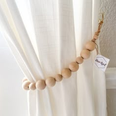 a wooden beaded necklace hanging from the side of a curtain with a name tag attached to it