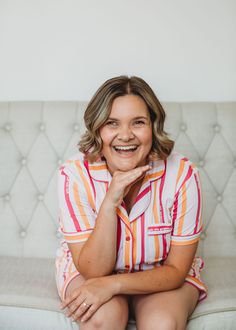 a woman sitting on top of a couch smiling at the camera with her hand under her chin