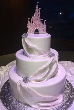 a three tiered white cake with a castle on top and ribbons around the edges