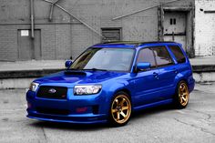 a blue subaru with gold rims parked in front of a brick building