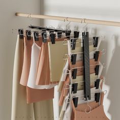 clothes hanging on a rack in front of a white wall and beige curtains with black clips attached to them