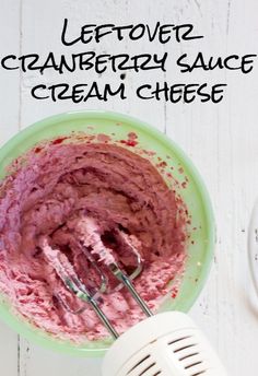 a green bowl filled with pink cream next to a whisk on top of a white table