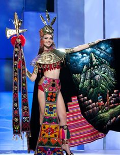 a woman in a costume is holding a large piece of art on the catwalk