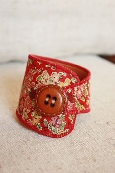 a close up of a button on a red flowered fabric cuff with a wooden button