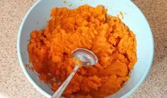 a bowl filled with mashed carrots on top of a counter next to a spoon