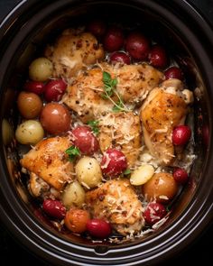 a crock pot filled with chicken, potatoes and red grapes next to some parmesan cheese