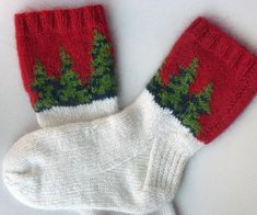 two red and white knitted mittens with green leaves on them sitting next to each other