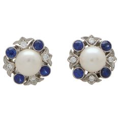 An extremely elegant pair of pearl, diamond and blue sapphire cluster earrings in 18k white gold. Each earring centrally features a lustrous white cultured pearl and is surrounded by an abstract halo of millegrain diamonds and blue sapphires. Both earrings are secured to reverse with a white gold post and butterfly fitting. Due to their design and size these earrings have so much versatility and could easily be worn for everyday or dressed up for more special occasions. The contrast between the blue sapphires against the pearls and diamonds is beautiful and makes the pair stand out more on the ear. There is a total diamond weight of 0.18 carats. These diamonds are estimated as G-H in colour with VVS clarity. There is a total blue sapphire weight of 0.40 carats, and they have all been beaut Blue Sapphire Diamond, Pearl Cluster, Pearl Diamond, Cluster Earrings, Pearl White, Pandora Charm Bracelet, Blue Sapphire, Halo, Pearl Earrings