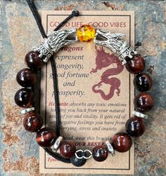 "Introducing the GOOD LIFE/GOOD VIBES bracelet! A bracelet that is beautiful and meaningful.    SYMBOLIC MEANING OF THIS BRACELET: 🔥 Dragons are symbols of prosperity, success and good luck.   The positive energy from this bracelet helps you LIVE YOUR BEST LIFE! This POWERFUL bracelet:   👍 Features SiLVER dragon head beads, 👍 🔥 FIRE DRAGON (red & yellow central bead) or 🧊 ICE DRAGON (clear central bead), 👍 Has 10mm Red Tiger's Eye Beads interspersed with grey Hematite spacer Beads, 👍 Is m Spiritual Charm Bracelet With 8mm Beads As A Gift, Amber Spiritual Bracelets For Meditation, Spiritual Good Luck Charm Bracelet, Brown Hand Wrapped Stretch Bracelet For Gift, Brown Hand Wrapped Stretch Bracelet Gift, Spiritual Nickel-free Beaded Bracelets As A Gift, Nickel Free Spiritual Beaded Bracelets As Gift, Nickel-free Spiritual Beaded Bracelets Gift, Hand-strung Spiritual Charm Bracelet As Gift