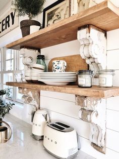 a kitchen shelf filled with lots of dishes on top of white counter tops next to a potted plant