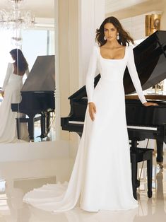 a woman standing in front of a piano wearing a long white dress with sleeves down