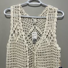 a white crocheted vest hanging on a hanger next to a gray wall