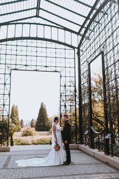 a bride and groom standing under an iron structure