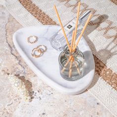 a white marble tray with rings and candles on it, next to a glass bottle