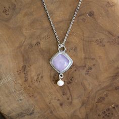 New! Purple Chalcedony Dyna Necklace. Gorgeous and unique Soft, Cool Violet Purple Chalcedony Cushion Square Cabochon is set tipped like a diamond in.925 Sterling Silver - paired with a lustrous, freshwater pearl dangle. All .925 Sterling Silver - includes .925 Sterling Silver chain. We've tipped the square like a diamond for dynamism, and to feature the stone in this new LBJ original. Dyna Necklace in Purple Chalcedony. With a minimal .925 Sterling Silver setting - this Purple Chalcedony Quartz Silver Jewelry With Square Pearl Pendant, Sterling Silver Pendant With Bezel Setting, Sterling Silver Pendant Jewelry With Bezel Setting, Sterling Silver Pendant Necklace With Bezel Setting, Anniversary White Gold Cabochon Necklace, Sterling Silver Cabochon Necklace For Anniversary, One Of A Kind Sterling Silver Necklaces For Anniversary, One Of A Kind Sterling Silver Necklace For Anniversary, Sterling Silver Cabochon Necklace Fine Jewelry