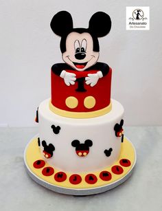 a mickey mouse cake with red and yellow decorations on the bottom tier, sitting on top of a white table