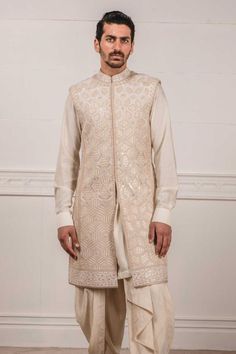 Ivory sleeveless sherwani with all-over applique, zardozi work paired with short kurta. Comes with dhoti pants.
Components:3
Embroidered
Neckline:Mandarin Collar
Sleeve Length:Kurta: Full; Sherwani: Sleeveless
Fabric:Katan silk, Raw silk
Color:White
Cuff sleeves
Side slits
Closure: Sherwani: Concealed front placket - Aza Fashions Elegant White Chanderi Nehru Jacket, Traditional Sleeveless Kurta For Reception, Sleeveless Kurta For Eid Reception, Festive Naqshi Bandhgala In Chanderi, White Sleeveless Kurta With Zari Work, Sleeveless Nehru Jacket With Resham Embroidery For Eid, Nehru Jacket With Naqshi For Reception, Straight Kurta, Straight Kurta Nehru Jacket With Intricate Embroidery For Reception, Reception Nehru Jacket With Intricate Embroidery