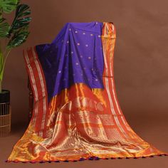 Regal as a royal twilight, the purple Gadwal silk saree unfurled its majesty, all-over woven zari polka buttas shimmering like starry night skies. Gold zari woven orange border and pallu blazed like vibrant sunsets, while the orange blouse added a touch of fiery elegance. Together, they created a canvas of dramatic splendor, a celebration of life's bold moments. She who wore this saree was a queen, her beauty and grace as commanding as a royal procession, her spirit as fiery as a blazing sun, illuminating all in her presence with radiant confidence and poise * Gadwal silk saree for special occasions. * Crafted from the premium quality fabric. * Supplied with a readymade blouse. * The blouse comes with an added allowance, and it can be altered to a standard size of 34"-42" on request. * Dry Royal Silk Saree, Purple Bollywood Style Paithani Silk Blouse Piece, Purple Paithani Silk Bollywood Blouse Piece, Bollywood Style Purple Paithani Silk Blouse Piece, Purple Paithani Silk Handloom Blouse Piece, Purple Paithani Silk Blouse Piece For Diwali, Diwali Paithani Silk Purple Blouse Piece, Purple Saree For Eid Celebration, Purple Traditional Wear For Celebration