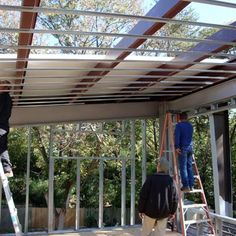 two men are working on the roof of a house that's being built with metal framing