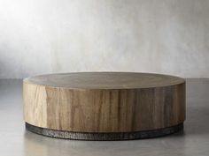 a round wooden table sitting on top of a cement floor next to a white wall