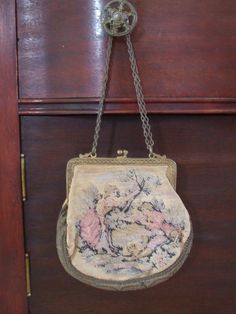 A charming piece of history, this petite French handbag was made around the turn of the 20th century  and is intricately detailed.  Both sides of the handbag are brocade, and capture an afternoon in the French countryside.  It is embroidered in muted rose, greens, blues, mustard and yellow all on a ecru background.  The bottom and edges are a  heavy trim material of 'patina'ed bronze with gold threads still peeking through. The opening of the bag is framed with brass that has a pressed floral de Vintage Evening Bag In Tapestry Material, Vintage Tapestry Bag For Evening, Vintage Tapestry Bag For Formal Occasions, Vintage Tapestry Shoulder Bag For Evening, Vintage Formal Tapestry Bag, Vintage Tapestry Pouch Bag, Formal Vintage Tapestry Bag, Antique Tapestry Evening Bag, Antique Tapestry Bags For Everyday