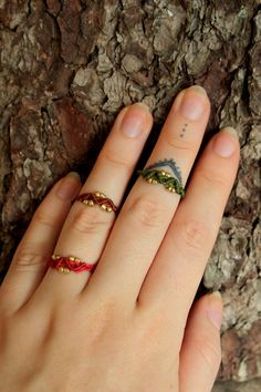 a woman's hand with three rings on it, next to a tree trunk