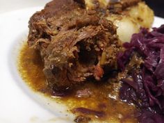 a white plate topped with meat, potatoes and red cabbage next to gravy