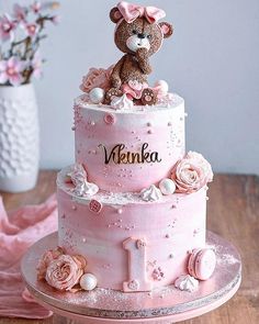 a pink birthday cake with a teddy bear on top and flowers in the bottom tier