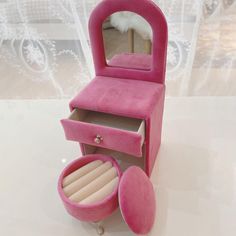 a small pink vanity with mirror and jewelry box on it's side, sitting on a table