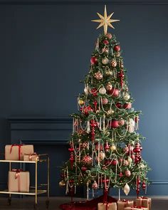 a christmas tree with presents under it in front of a blue wall and wooden floor