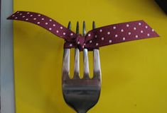 a fork with a polka dot ribbon on it is attached to a yellow wall,