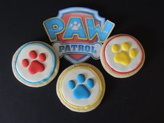 three decorated cookies with paw patrol logo on top and dog's footprints in the middle