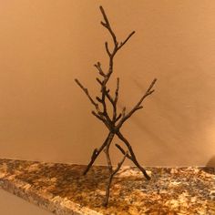 a small tree made out of branches sitting on top of a marble counter next to a wall