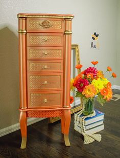 an orange chest of drawers next to a vase with flowers