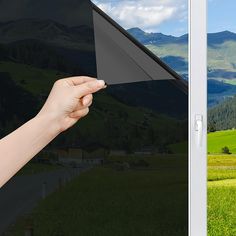 a hand is holding an electronic device in front of a mountain landscape with green grass