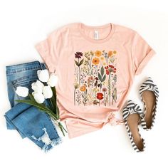 a t - shirt with a dandelion design on it next to shoes and flowers